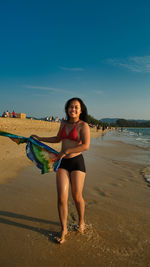 Portrait of young woman standing at beach against sky