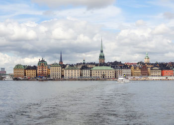 View of buildings by river against cloudy sky