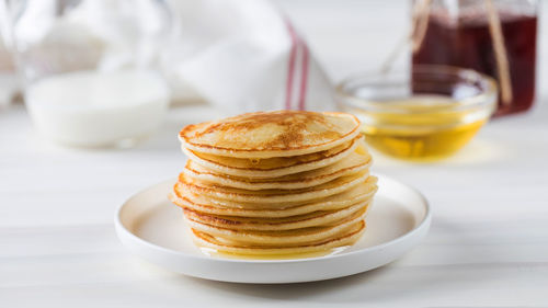 The pancakes are stacked in a plate. in the background, a bowl of honey and a jug of milk.