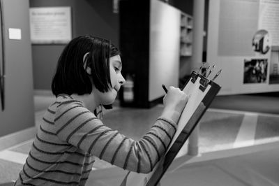 Girl drawing on clipboard at museum