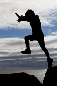 Silhouette of man with arms raised against cloudy sky