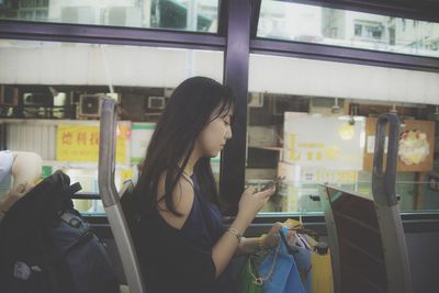 Side view of young woman using smart phone while sitting in public transportation