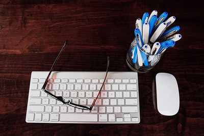 High angle view of keyboard with mouse and pens on wooden table