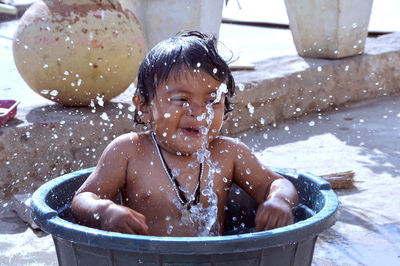 Shirtless baby boy splashing water in bucket
