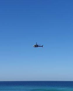 Helicopter hovering over water against clear blue sky