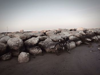 Bicycle parked by rocks against clear sky