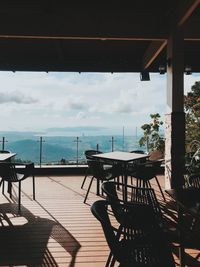 Empty chairs and tables by sea against sky