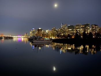 Illuminated buildings by river against sky at night