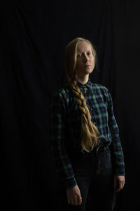 Portrait of young woman standing against black background