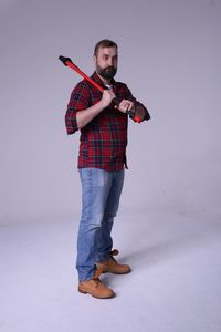 Full length of lumberjack holding axe while standing against white background