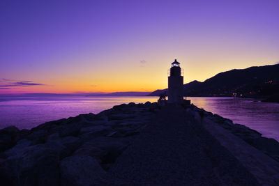 Lighthouse on beach by sea against sky during sunset