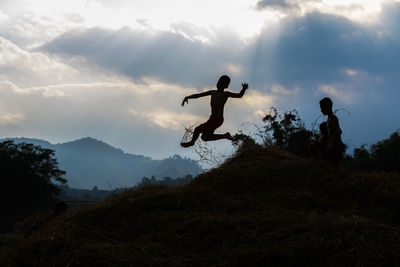 Silhouette children jumping on hay against sky
