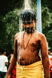 Shirtless man taking shower while standing outdoors