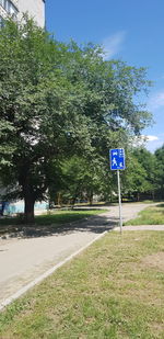 Road sign by trees against sky