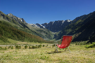 Empty chair on field by mountains against blue sky