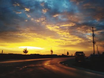 Cars on road against dramatic sky during sunset