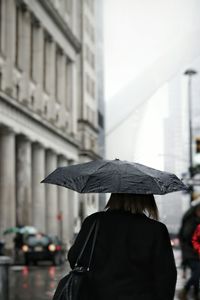 Rear view of woman walking with umbrella on street during rainy season