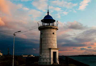 Lighthouse by sea against sky during sunset