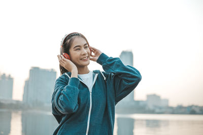 Portrait of smiling young woman in city against sky