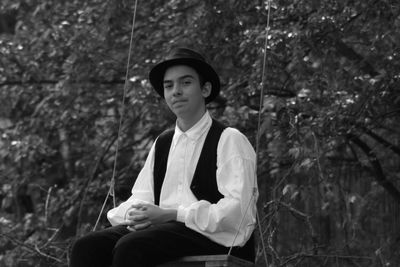 Portrait of teenage boy sitting on swing against plants