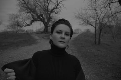 Portrait of beautiful young woman standing against bare trees