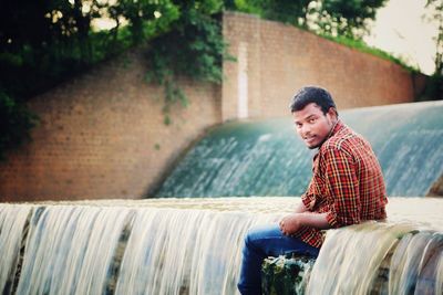 Portrait of young man sitting at waterfall