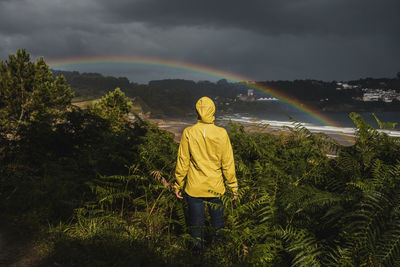 Rear view of man standing against rainbow in sky