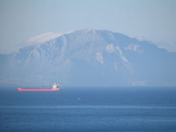 Container ship sailing in sea by mountain against sky