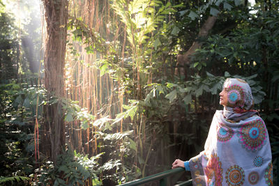 Rear view of woman standing by plants in forest