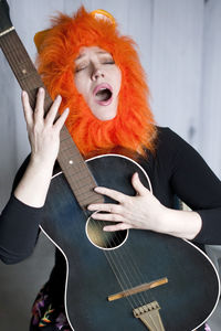 Middle-aged woman wearing lion wig, singing song with her mouth open and playing the guitar