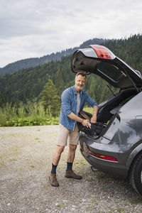 Smiling mature man packing bag while standing by car