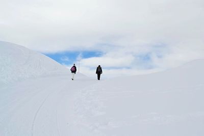 Rear view of people walking on snow covered hill against cloudy sky