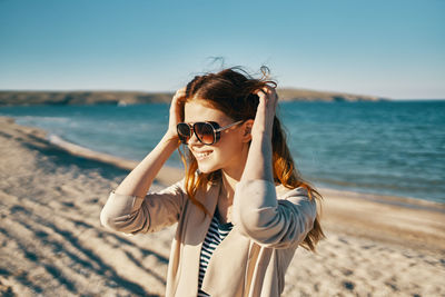 Young woman wearing sunglasses on beach against sky