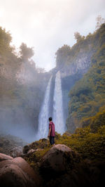 Man standing on rock looking at waterfall