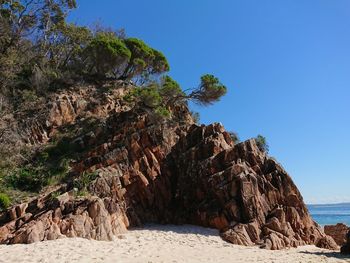 Rock formation by sea against clear blue sky