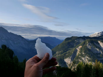 Person hand holding mountain against sky