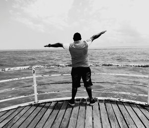 Rear view of man standing on sea shore against sky