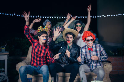 Portrait of young friends in costume holding cutouts during party