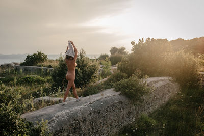 Naked woman walking on railing against sky during sunset