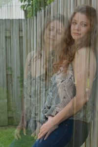 Portrait of young woman standing by glass