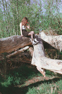 Young woman sitting on fallen tree at forest