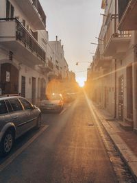 Cars on road by buildings against sky during sunset