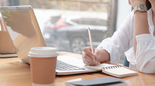 Midsection of woman holding coffee cup on table