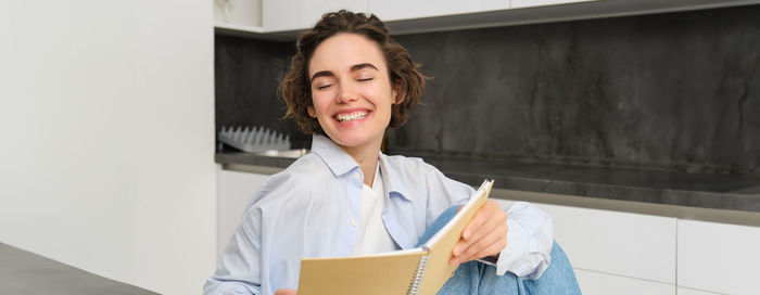 Portrait of young woman using digital tablet while standing against wall