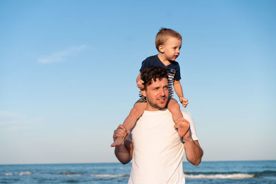 Father and son enjoying at beach against sky