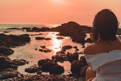 Rear view of woman sitting at beach against clear sky during sunset