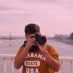 Man photographing with camera against sky during sunset