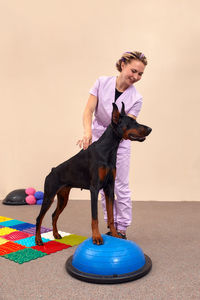 Portrait of young woman with dog standing against wall