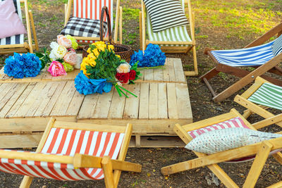 Beautiful artificial bouquets of various colors placed on wooden table among deck chairs in garden. 