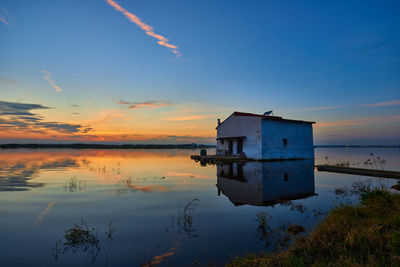 House by lake against sky during sunset